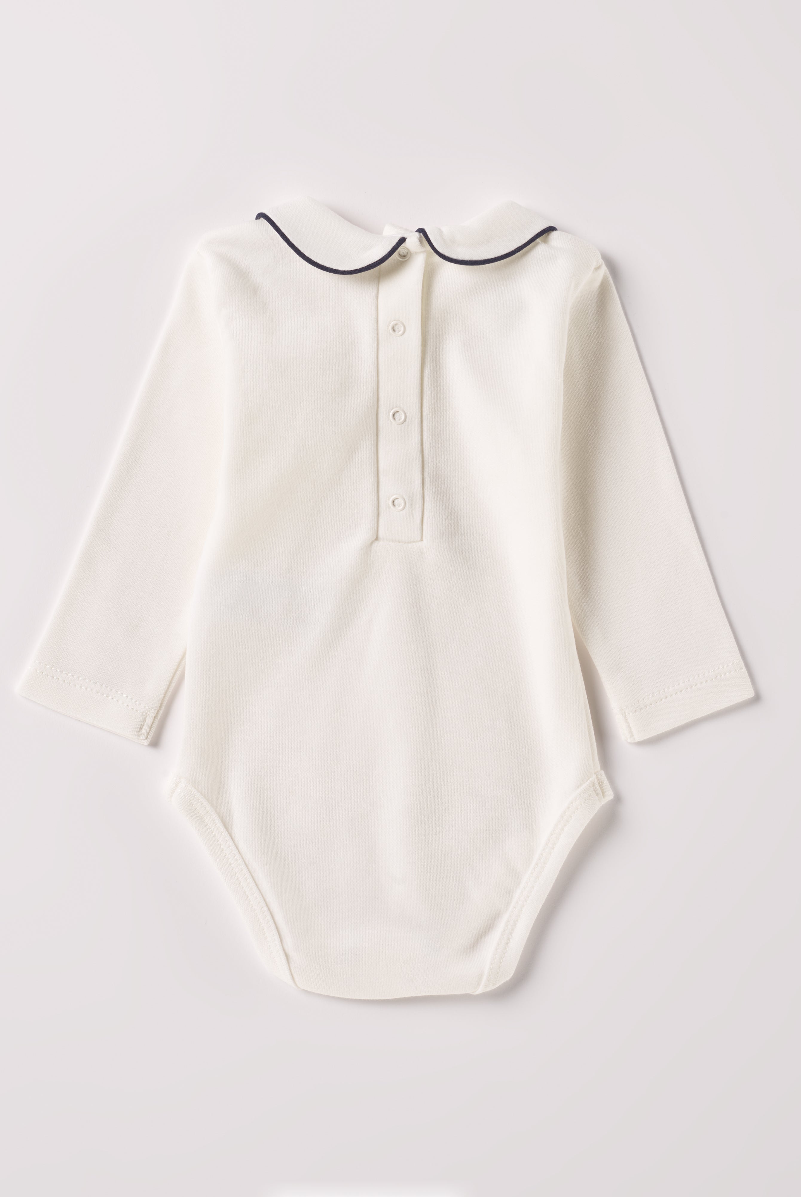Der langarmige Body, gefertigt aus 100% Baumwolle, hat eine perfekte Passform. Kundinnen und Kunden vertrauen auf unseren Schnitt, da die flachen Druckknöpfe an der Rückseite ein unkompliziertes und schnelles Anziehen ermöglichen. Die "flanellartige" Innenseite wurde speziell für zarte Kinderhaut konzipiert und bietet ein besonders sanftes Trageerlebnis. Ein großer Vorteil der flanellartigen Innenseite ist, dass die Kinder weniger schwitzen. Der Kragen verleiht dem Body ein edles Design.