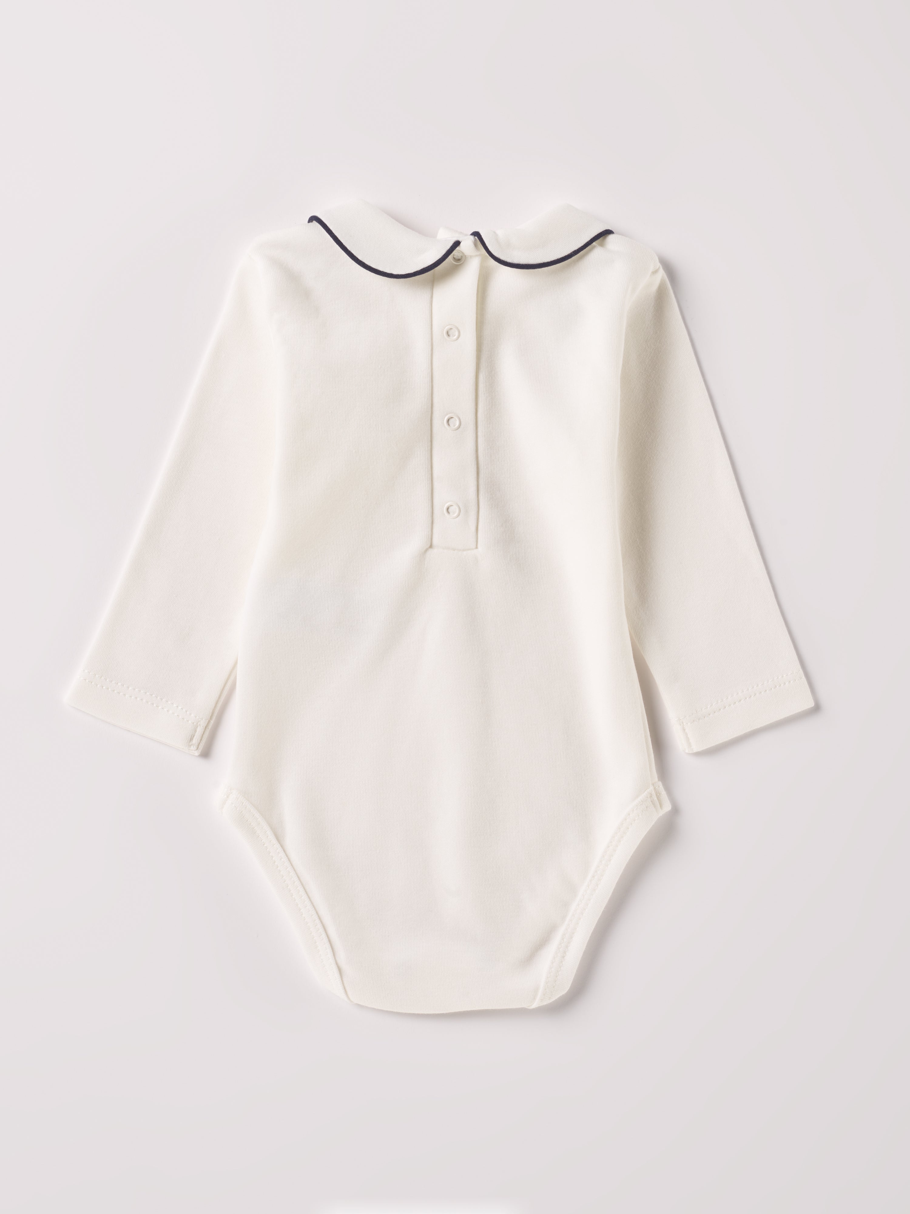 Der langarmige Body, gefertigt aus 100% Baumwolle, hat eine perfekte Passform. Kundinnen und Kunden vertrauen auf unseren Schnitt, da die flachen Druckknöpfe an der Rückseite ein unkompliziertes und schnelles Anziehen ermöglichen. Die "flanellartige" Innenseite wurde speziell für zarte Kinderhaut konzipiert und bietet ein besonders sanftes Trageerlebnis. Ein großer Vorteil der flanellartigen Innenseite ist, dass die Kinder weniger schwitzen. Der Kragen verleiht dem Body ein edles Design.