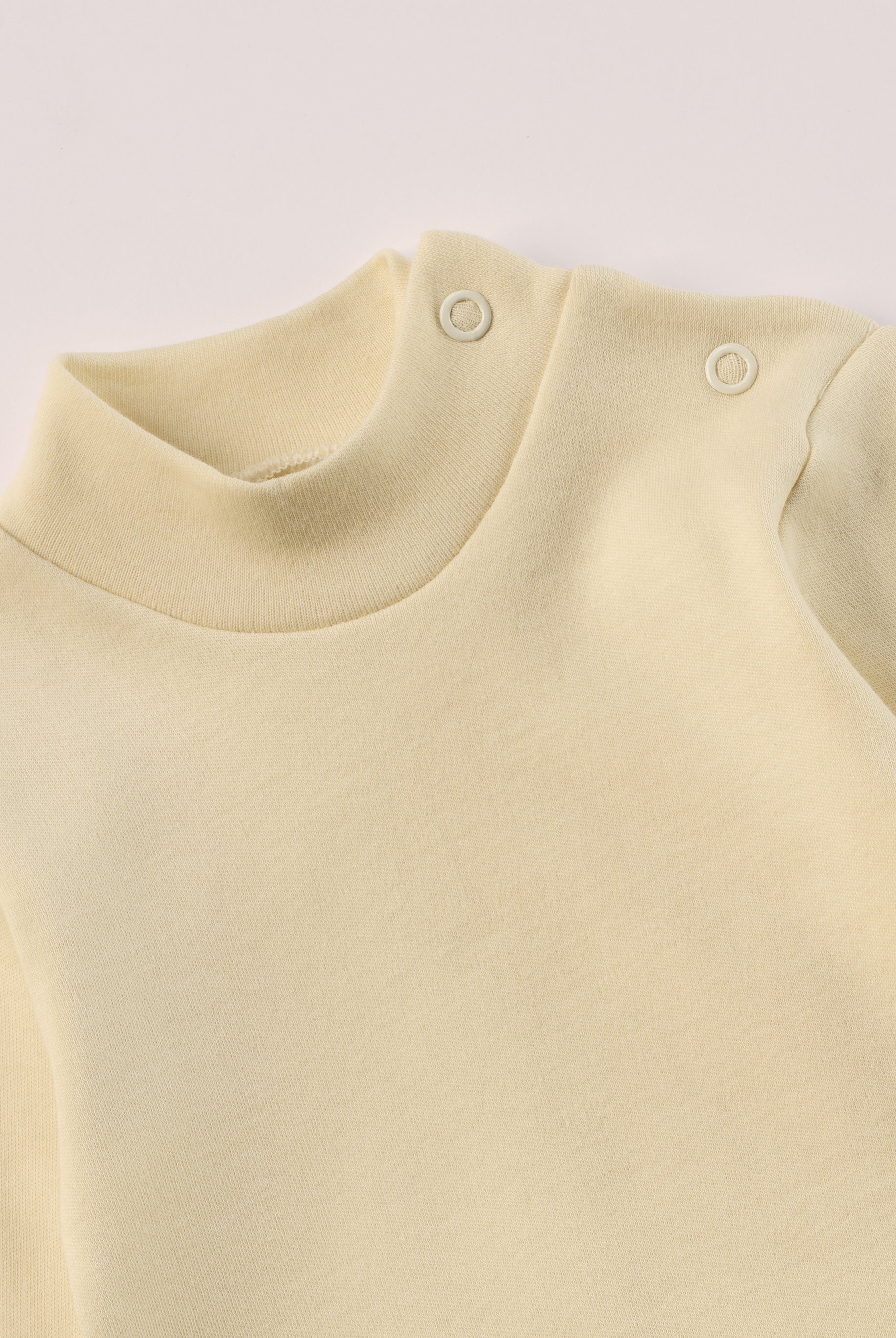 Dieser beige Stehkragenbody besteht aus hochwertiger, sorgfältig veredelter organischer Baumwolle. Die Stoffe sind sanft gefärbt und gebleicht unter Einhaltung strenger EU-Standards. Die nickelfreien Druckknöpfe an der Schulterpartie machen das An- und Ausziehen unkompliziert und schnell.
Innen sorgt die weich angeraute Oberfläche für angenehme Wärme, Feuchtigkeitsaufnahme und ein sanftes Hautgefühl. Der schützende Stehkragen hält den empfindlichen Halsbereich warm und reduziert Zugluft.
