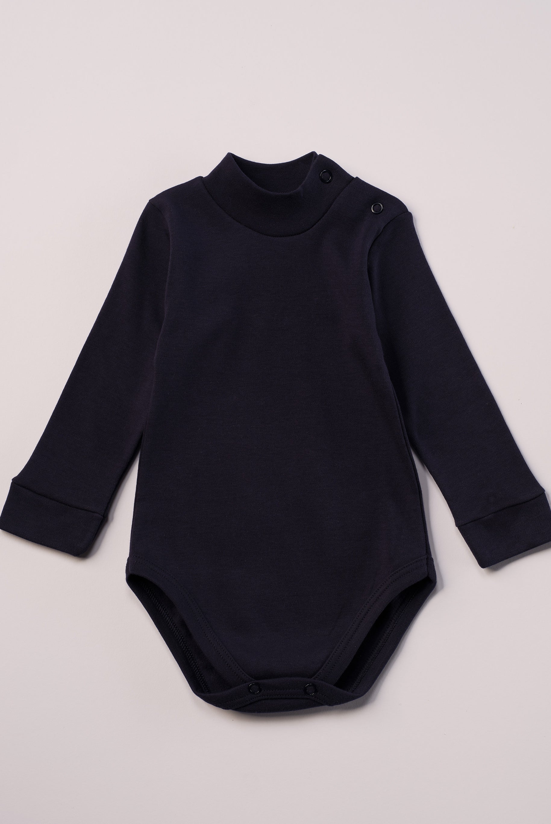 Dieser blaue Stehkragenbody besteht aus hochwertiger, sorgfältig veredelter organischer Baumwolle. Die Stoffe sind sanft gefärbt und gebleicht unter Einhaltung strenger EU-Standards. Die nickelfreien Druckknöpfe an der Schulterpartie machen das An- und Ausziehen unkompliziert und schnell.
Innen sorgt die weich angeraute Oberfläche für angenehme Wärme, Feuchtigkeitsaufnahme und ein sanftes Hautgefühl. Der schützende Stehkragen hält den empfindlichen Halsbereich warm und reduziert Zugluft.