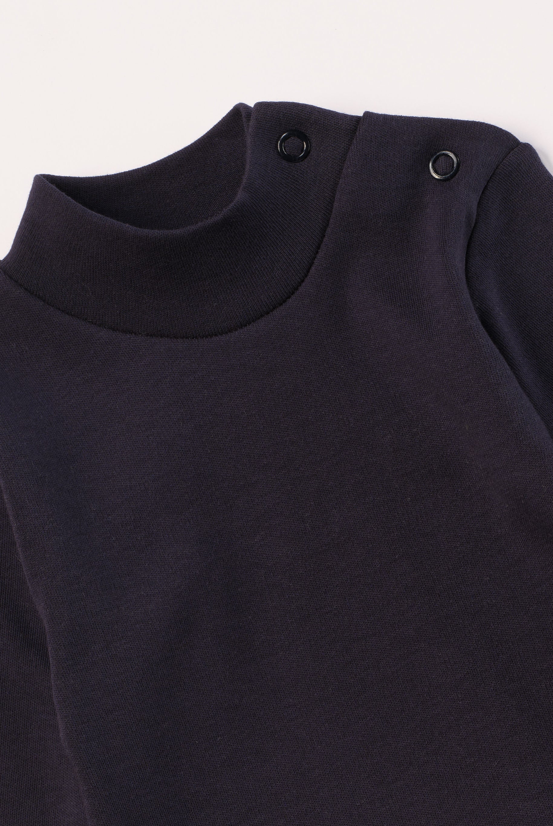 Dieser blaue Stehkragenbody besteht aus hochwertiger, sorgfältig veredelter organischer Baumwolle. Die Stoffe sind sanft gefärbt und gebleicht unter Einhaltung strenger EU-Standards. Die nickelfreien Druckknöpfe an der Schulterpartie machen das An- und Ausziehen unkompliziert und schnell.
Innen sorgt die weich angeraute Oberfläche für angenehme Wärme, Feuchtigkeitsaufnahme und ein sanftes Hautgefühl. Der schützende Stehkragen hält den empfindlichen Halsbereich warm und reduziert Zugluft.