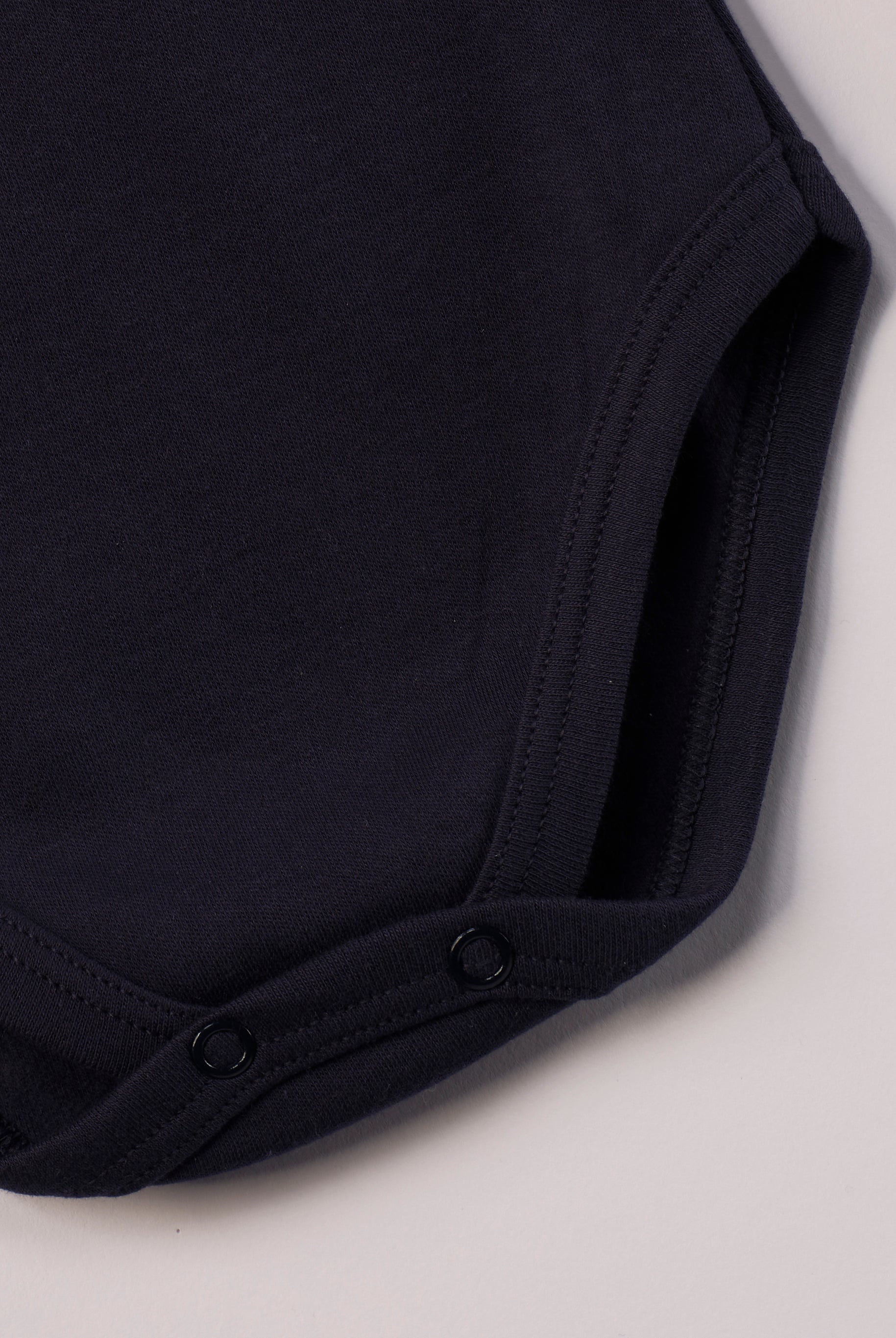 Dieser blaue Stehkragenbody besteht aus hochwertiger, sorgfältig veredelter organischer Baumwolle. Die Stoffe sind sanft gefärbt und gebleicht unter Einhaltung strenger EU-Standards. Die nickelfreien Druckknöpfe an der Schulterpartie machen das An- und Ausziehen unkompliziert und schnell.
Innen sorgt die weich angeraute Oberfläche für angenehme Wärme, Feuchtigkeitsaufnahme und ein sanftes Hautgefühl. Der schützende Stehkragen hält den empfindlichen Halsbereich warm und reduziert Zugluft.