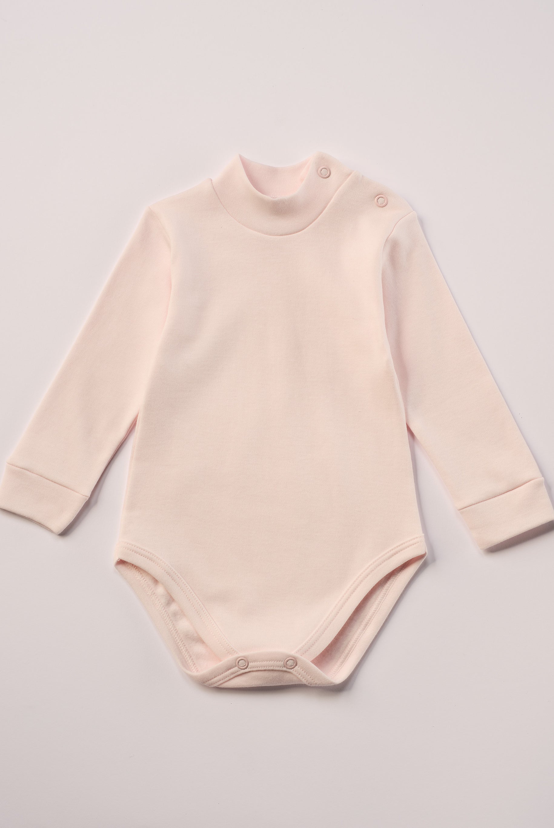 Dieser rosa Stehkragenbody besteht aus hochwertiger, sorgfältig veredelter organischer Baumwolle. Die Stoffe sind sanft gefärbt und gebleicht unter Einhaltung strenger EU-Standards. Die nickelfreien Druckknöpfe an der Schulterpartie machen das An- und Ausziehen unkompliziert und schnell.
Innen sorgt die weich angeraute Oberfläche für angenehme Wärme, Feuchtigkeitsaufnahme und ein sanftes Hautgefühl. Der schützende Stehkragen hält den empfindlichen Halsbereich warm und reduziert Zugluft.