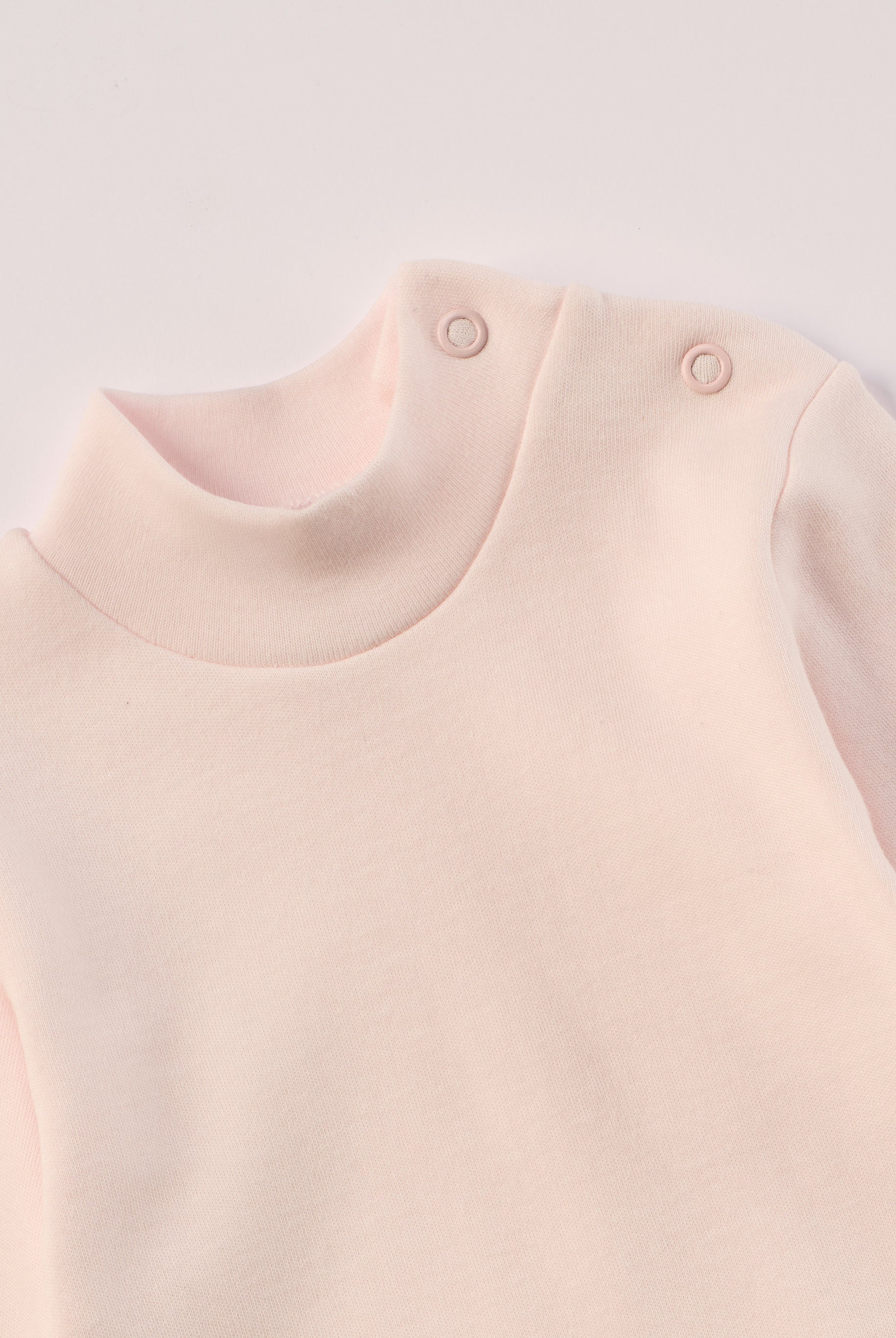 Dieser rosa Stehkragenbody besteht aus hochwertiger, sorgfältig veredelter organischer Baumwolle. Die Stoffe sind sanft gefärbt und gebleicht unter Einhaltung strenger EU-Standards. Die nickelfreien Druckknöpfe an der Schulterpartie machen das An- und Ausziehen unkompliziert und schnell.
Innen sorgt die weich angeraute Oberfläche für angenehme Wärme, Feuchtigkeitsaufnahme und ein sanftes Hautgefühl. Der schützende Stehkragen hält den empfindlichen Halsbereich warm und reduziert Zugluft.