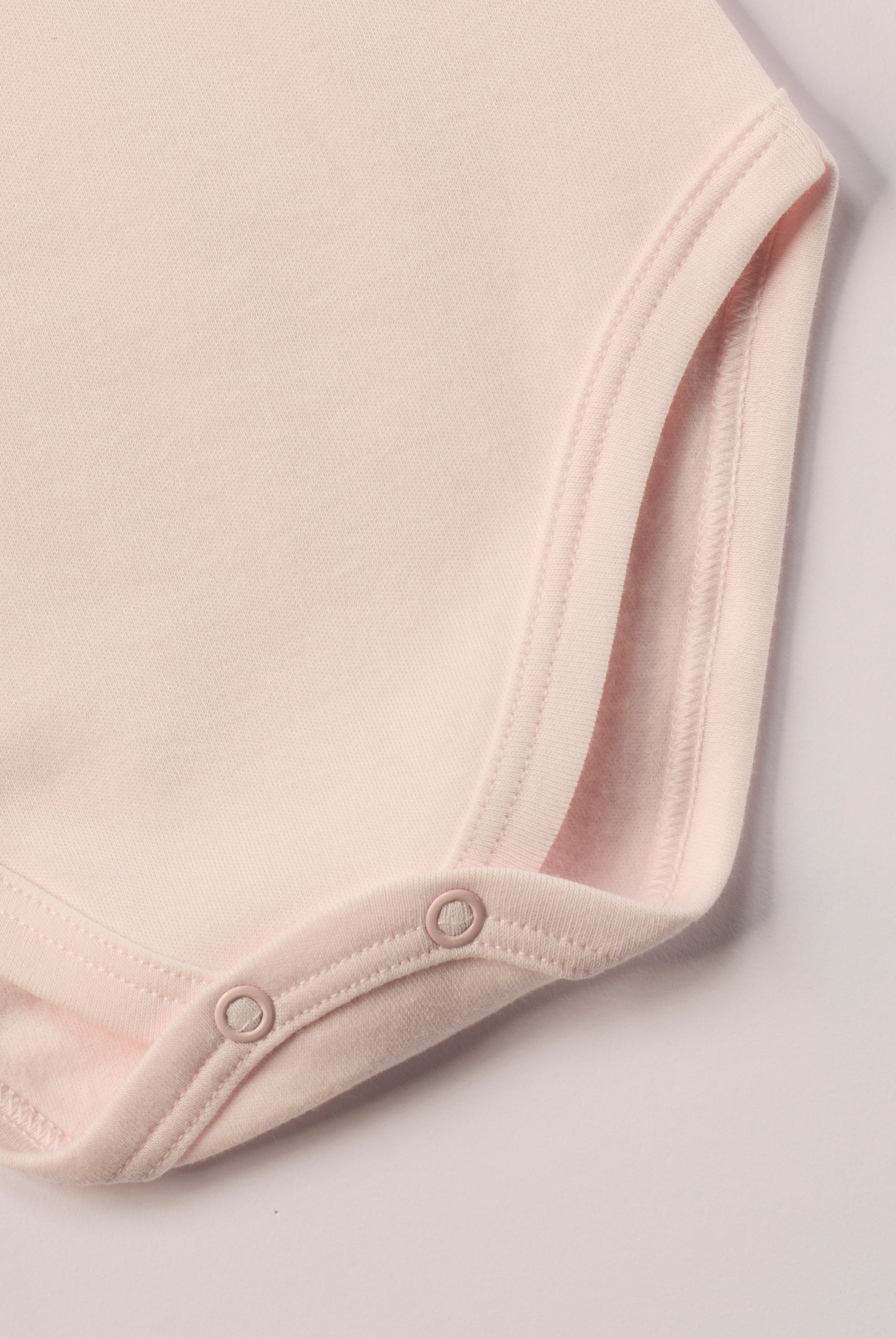 Dieser rosa Stehkragenbody besteht aus hochwertiger, sorgfältig veredelter organischer Baumwolle. Die Stoffe sind sanft gefärbt und gebleicht unter Einhaltung strenger EU-Standards. Die nickelfreien Druckknöpfe an der Schulterpartie machen das An- und Ausziehen unkompliziert und schnell.
Innen sorgt die weich angeraute Oberfläche für angenehme Wärme, Feuchtigkeitsaufnahme und ein sanftes Hautgefühl. Der schützende Stehkragen hält den empfindlichen Halsbereich warm und reduziert Zugluft.