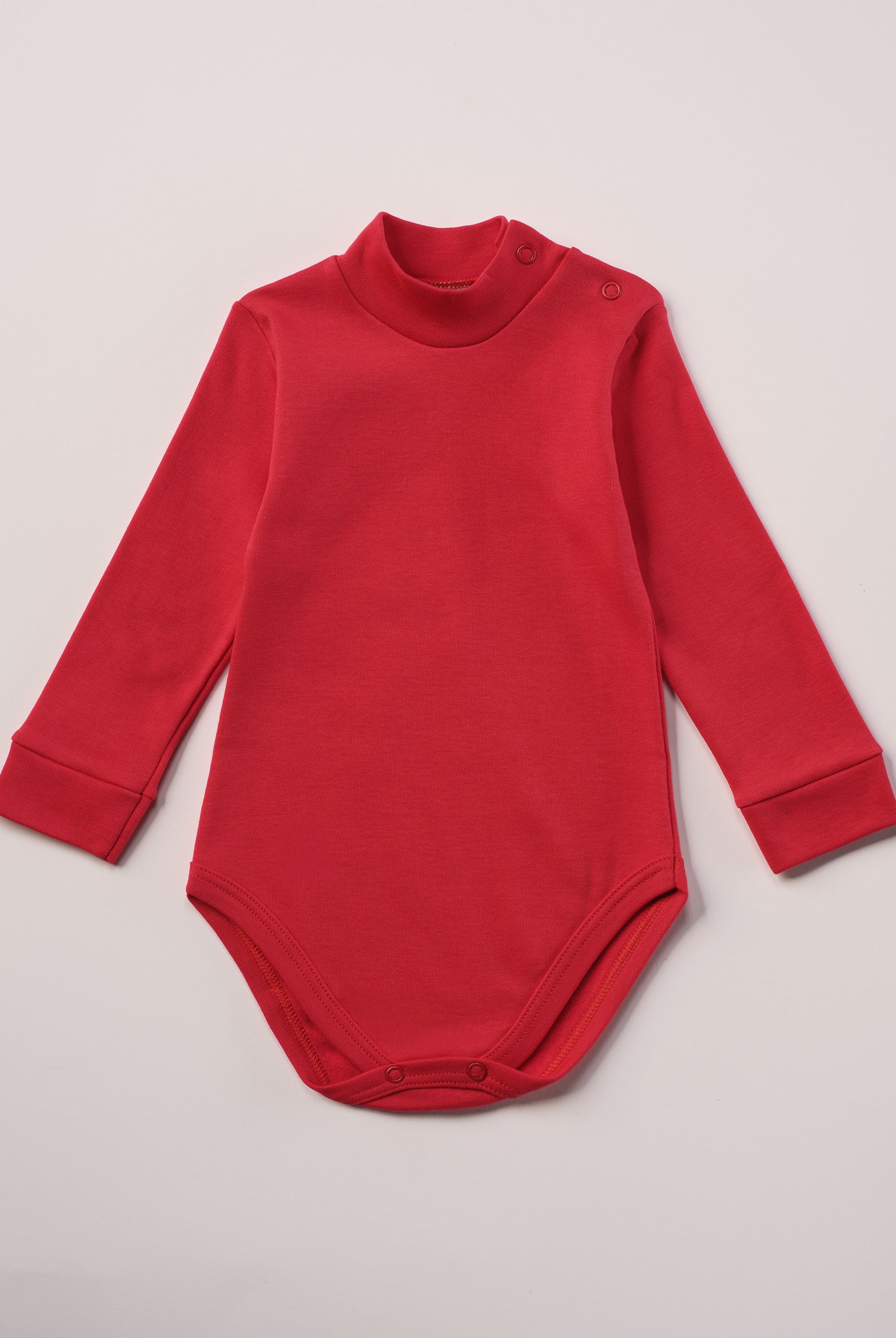 Dieser rote Stehkragenbody besteht aus hochwertiger, sorgfältig veredelter organischer Baumwolle. Die Stoffe sind sanft gefärbt und gebleicht unter Einhaltung strenger EU-Standards. Die nickelfreien Druckknöpfe an der Schulterpartie machen das An- und Ausziehen unkompliziert und schnell.
Innen sorgt die weich angeraute Oberfläche für angenehme Wärme, Feuchtigkeitsaufnahme und ein sanftes Hautgefühl. Der schützende Stehkragen hält den empfindlichen Halsbereich warm und reduziert Zugluft.