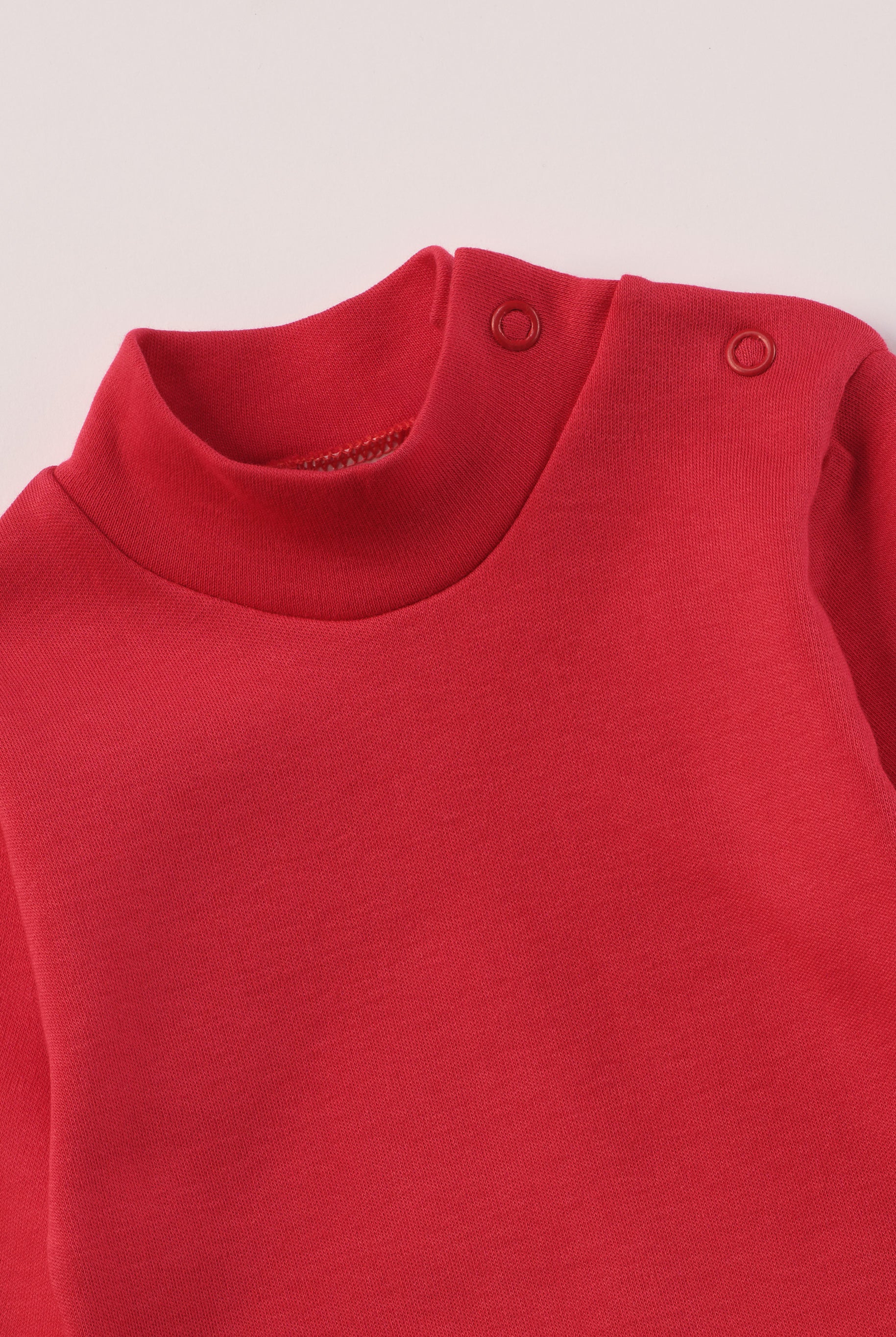 Dieser rote Stehkragenbody besteht aus hochwertiger, sorgfältig veredelter organischer Baumwolle. Die Stoffe sind sanft gefärbt und gebleicht unter Einhaltung strenger EU-Standards. Die nickelfreien Druckknöpfe an der Schulterpartie machen das An- und Ausziehen unkompliziert und schnell.
Innen sorgt die weich angeraute Oberfläche für angenehme Wärme, Feuchtigkeitsaufnahme und ein sanftes Hautgefühl. Der schützende Stehkragen hält den empfindlichen Halsbereich warm und reduziert Zugluft.