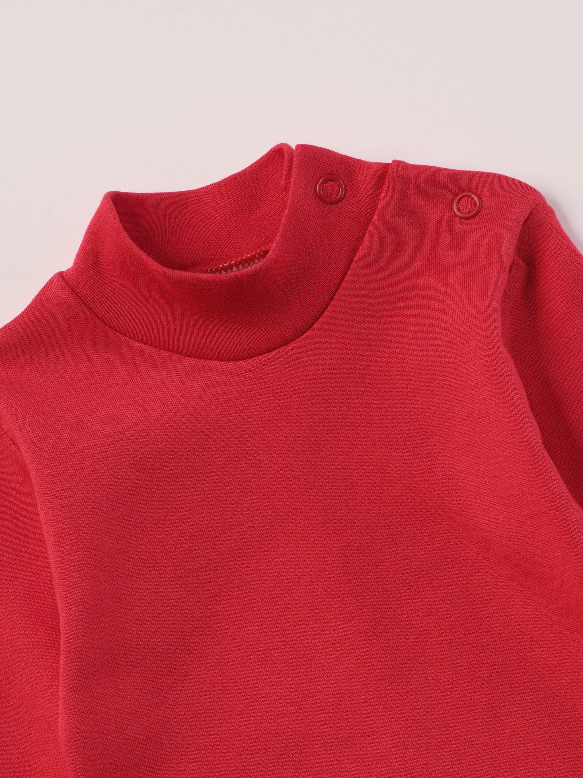 Dieser rote Stehkragenbody besteht aus hochwertiger, sorgfältig veredelter organischer Baumwolle. Die Stoffe sind sanft gefärbt und gebleicht unter Einhaltung strenger EU-Standards. Die nickelfreien Druckknöpfe an der Schulterpartie machen das An- und Ausziehen unkompliziert und schnell.
Innen sorgt die weich angeraute Oberfläche für angenehme Wärme, Feuchtigkeitsaufnahme und ein sanftes Hautgefühl. Der schützende Stehkragen hält den empfindlichen Halsbereich warm und reduziert Zugluft.