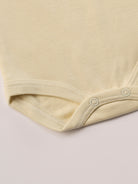 Für besonders sensible Babyhaut. Dieser beige Amerciano Body besteht aus hochwertiger Bambusviskose — einem Material, das für seine seidige Weichheit, hohe Atmungsaktivität und temperaturausgleichenden Eigenschaften bekannt ist. Sanft zur Haut, funktional im Alltag.