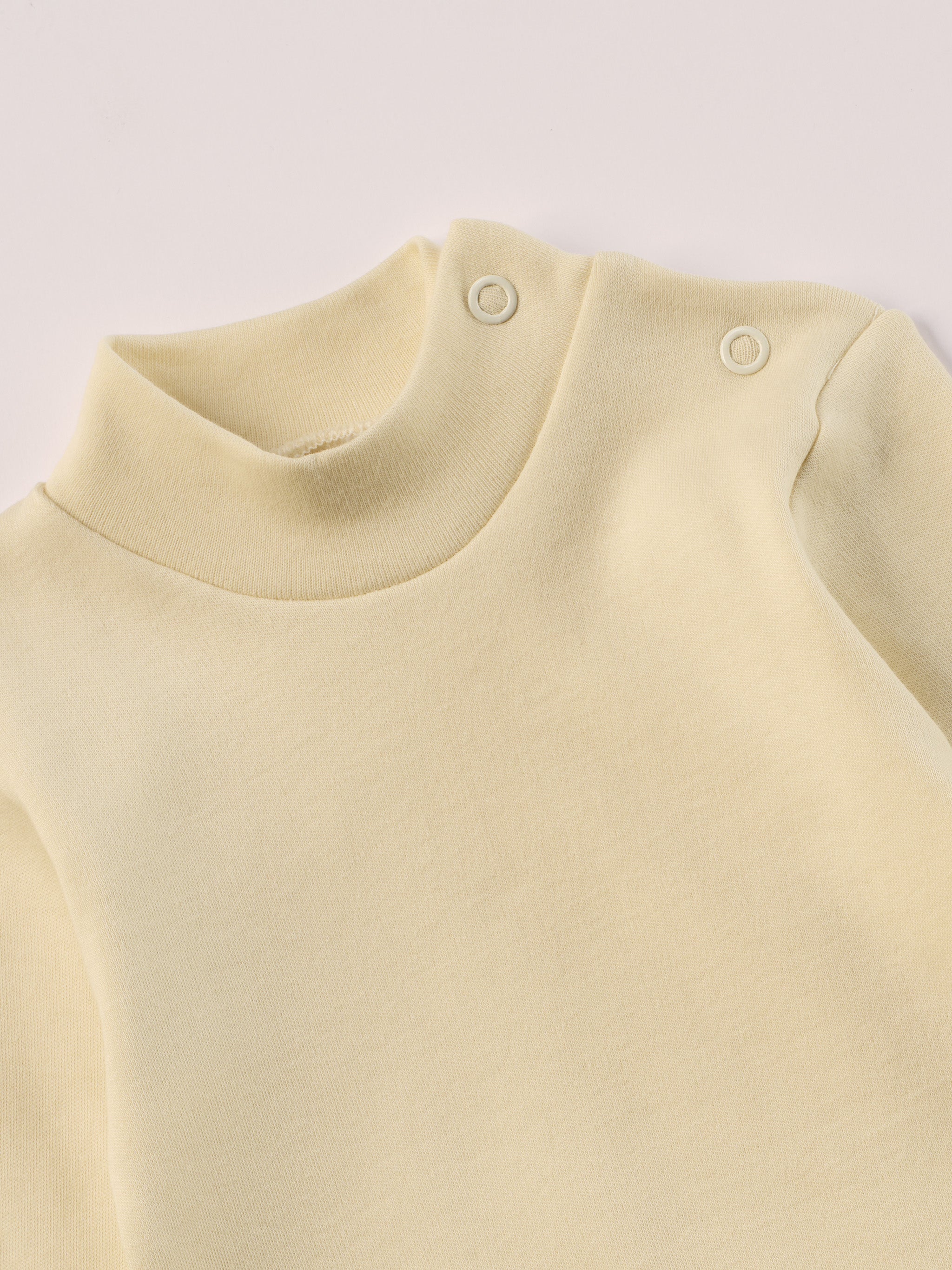 Dieser beige Stehkragenbody besteht aus hochwertiger, sorgfältig veredelter organischer Baumwolle. Die Stoffe sind sanft gefärbt und gebleicht unter Einhaltung strenger EU-Standards. Die nickelfreien Druckknöpfe an der Schulterpartie machen das An- und Ausziehen unkompliziert und schnell.

Innen sorgt die weich angeraute Oberfläche für angenehme Wärme, Feuchtigkeitsaufnahme und ein sanftes Hautgefühl. Der schützende Stehkragen hält den empfindlichen Halsbereich warm und reduziert Zugluft.