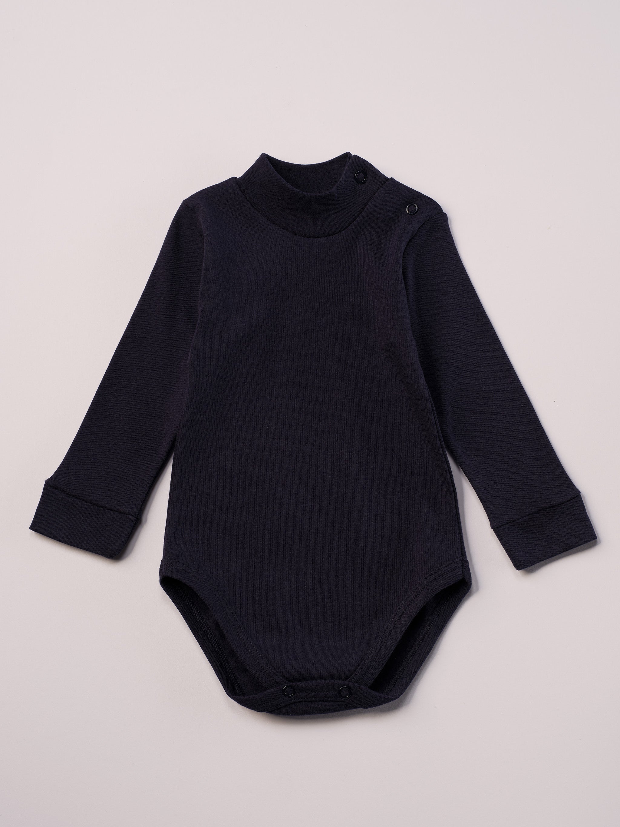 Dieser blaue Stehkragenbody besteht aus hochwertiger, sorgfältig veredelter organischer Baumwolle. Die Stoffe sind sanft gefärbt und gebleicht unter Einhaltung strenger EU-Standards. Die nickelfreien Druckknöpfe an der Schulterpartie machen das An- und Ausziehen unkompliziert und schnell.

Innen sorgt die weich angeraute Oberfläche für angenehme Wärme, Feuchtigkeitsaufnahme und ein sanftes Hautgefühl. Der schützende Stehkragen hält den empfindlichen Halsbereich warm und reduziert Zugluft.