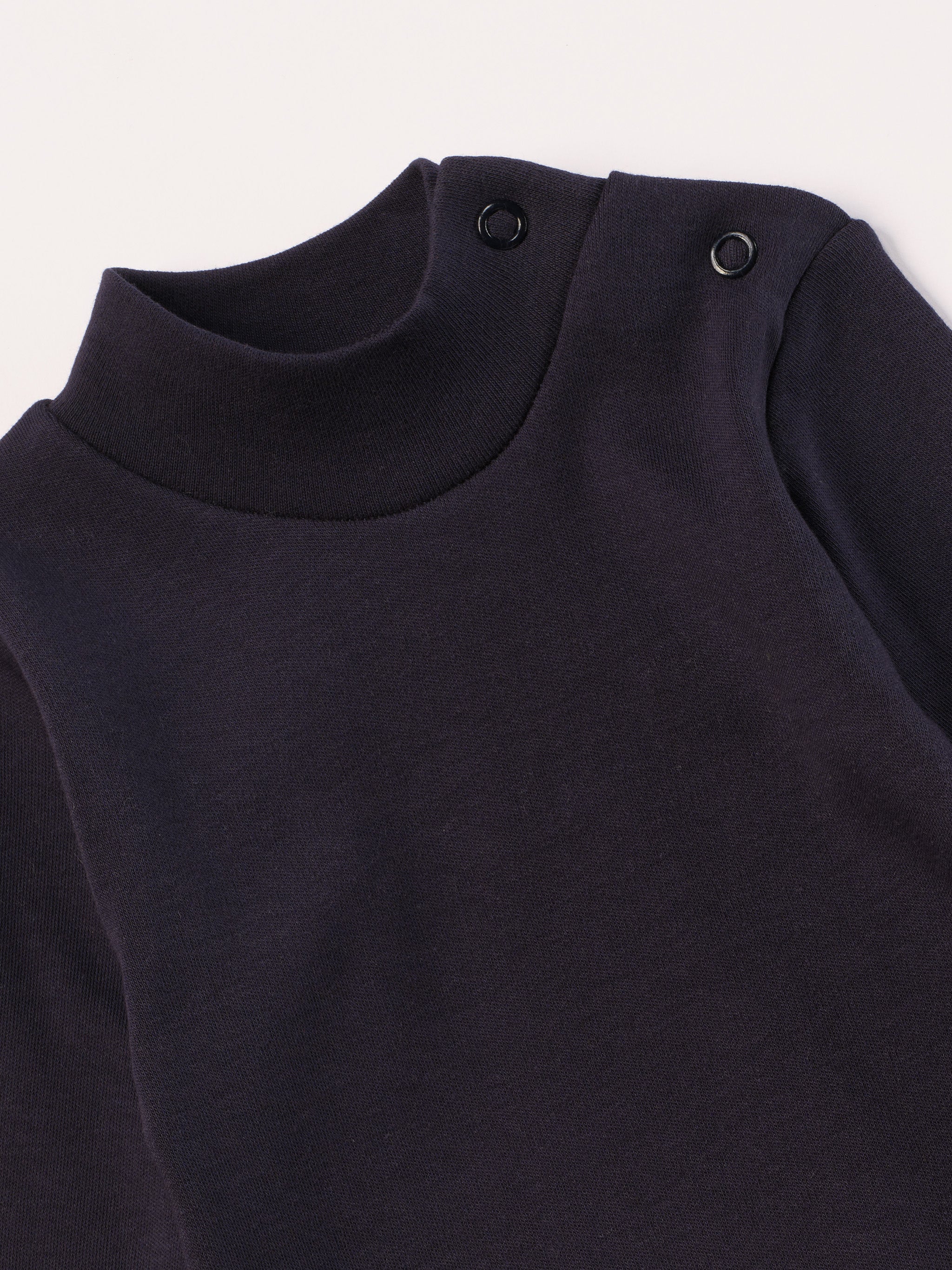 Dieser blaue Stehkragenbody besteht aus hochwertiger, sorgfältig veredelter organischer Baumwolle. Die Stoffe sind sanft gefärbt und gebleicht unter Einhaltung strenger EU-Standards. Die nickelfreien Druckknöpfe an der Schulterpartie machen das An- und Ausziehen unkompliziert und schnell.

Innen sorgt die weich angeraute Oberfläche für angenehme Wärme, Feuchtigkeitsaufnahme und ein sanftes Hautgefühl. Der schützende Stehkragen hält den empfindlichen Halsbereich warm und reduziert Zugluft.