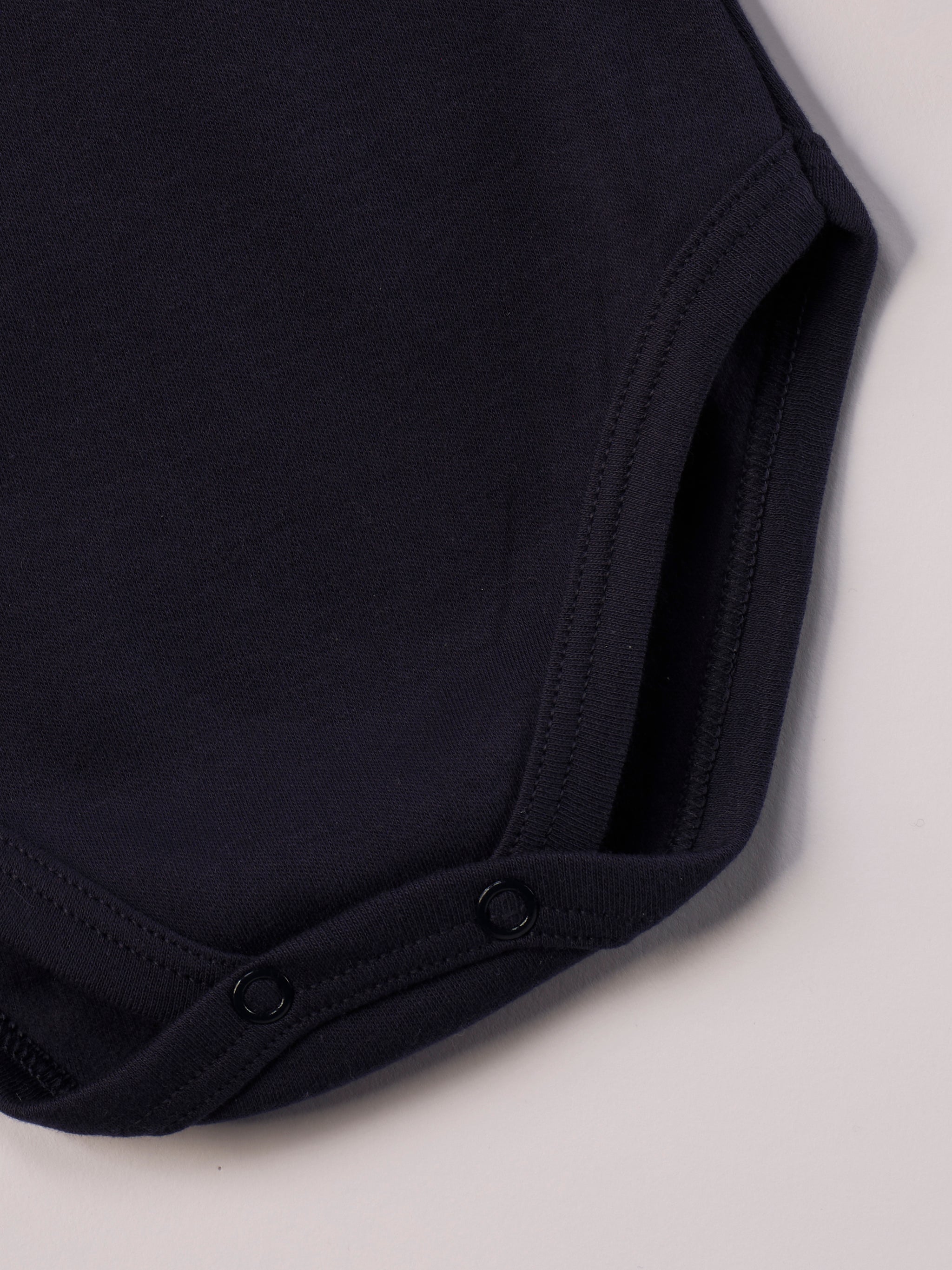 Dieser blaue Stehkragenbody besteht aus hochwertiger, sorgfältig veredelter organischer Baumwolle. Die Stoffe sind sanft gefärbt und gebleicht unter Einhaltung strenger EU-Standards. Die nickelfreien Druckknöpfe an der Schulterpartie machen das An- und Ausziehen unkompliziert und schnell.

Innen sorgt die weich angeraute Oberfläche für angenehme Wärme, Feuchtigkeitsaufnahme und ein sanftes Hautgefühl. Der schützende Stehkragen hält den empfindlichen Halsbereich warm und reduziert Zugluft.