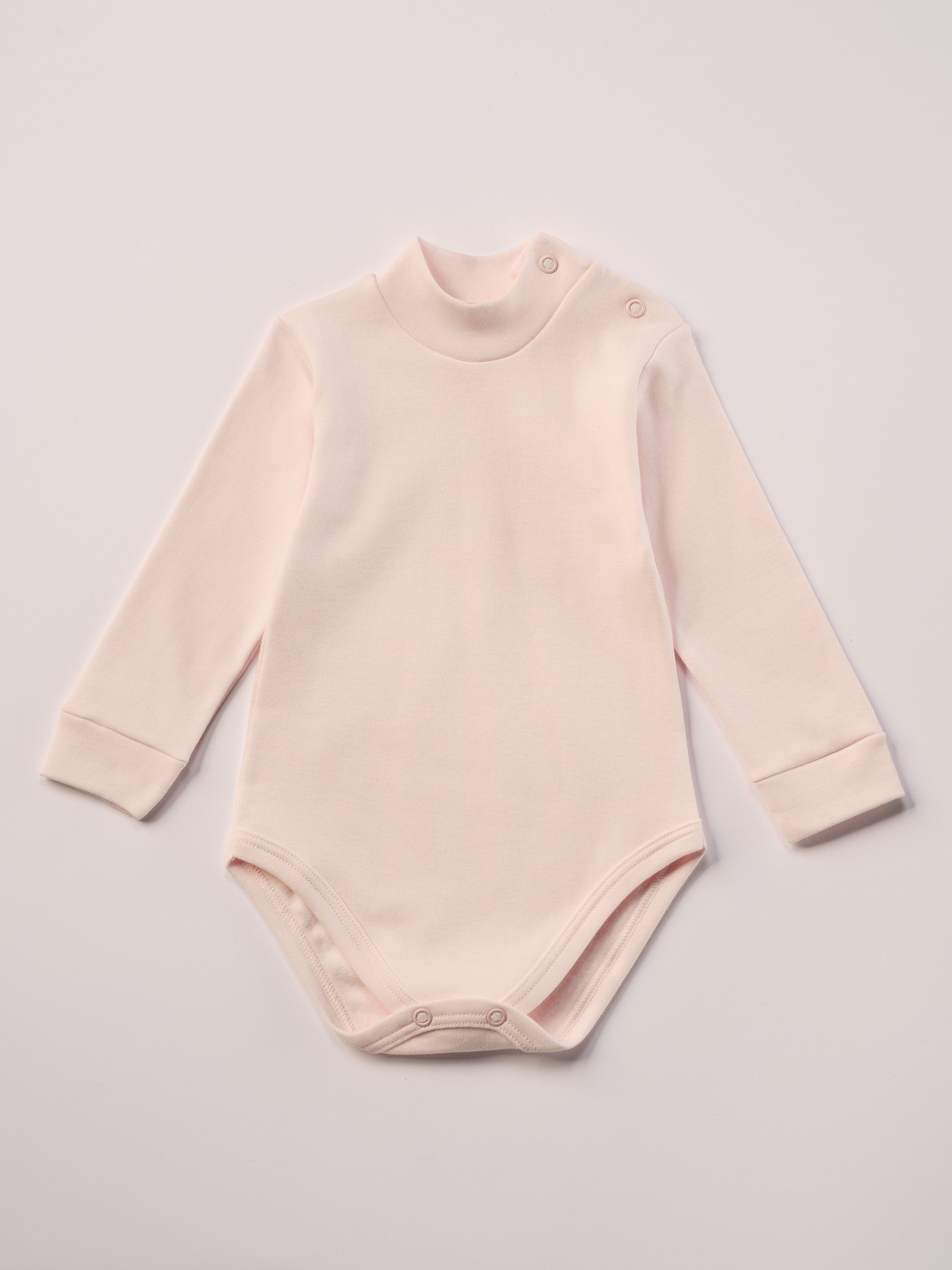 Dieser rosa Stehkragenbody besteht aus hochwertiger, sorgfältig veredelter organischer Baumwolle. Die Stoffe sind sanft gefärbt und gebleicht unter Einhaltung strenger EU-Standards. Die nickelfreien Druckknöpfe an der Schulterpartie machen das An- und Ausziehen unkompliziert und schnell.
Innen sorgt die weich angeraute Oberfläche für angenehme Wärme, Feuchtigkeitsaufnahme und ein sanftes Hautgefühl. Der schützende Stehkragen hält den empfindlichen Halsbereich warm und reduziert Zugluft.