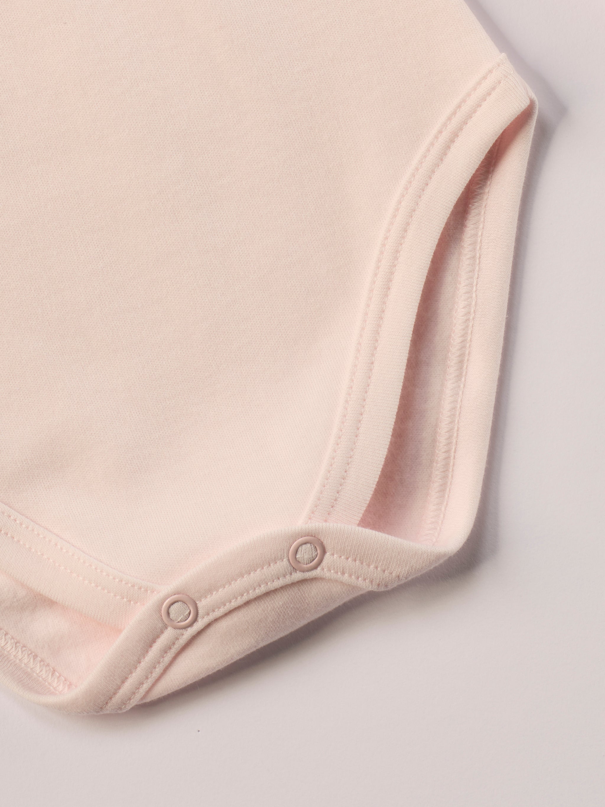 Dieser rosa Stehkragenbody besteht aus hochwertiger, sorgfältig veredelter organischer Baumwolle. Die Stoffe sind sanft gefärbt und gebleicht unter Einhaltung strenger EU-Standards. Die nickelfreien Druckknöpfe an der Schulterpartie machen das An- und Ausziehen unkompliziert und schnell.
Innen sorgt die weich angeraute Oberfläche für angenehme Wärme, Feuchtigkeitsaufnahme und ein sanftes Hautgefühl. Der schützende Stehkragen hält den empfindlichen Halsbereich warm und reduziert Zugluft.